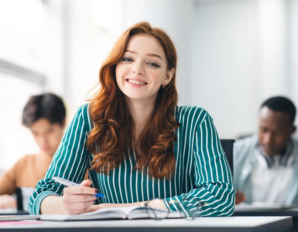 Smiling female student sitting at desk writing